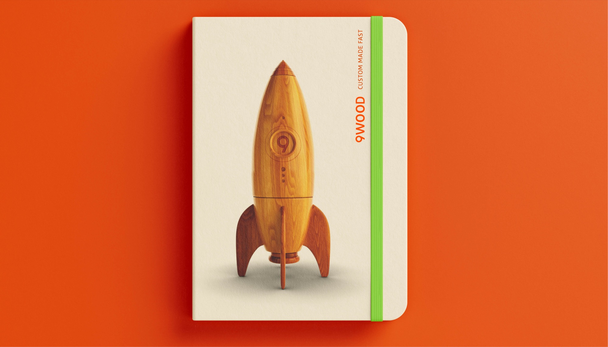 Cream notebook with the wooden rocket and a green elastic band, reading 9WOOD Custom made fast, on an orange ground