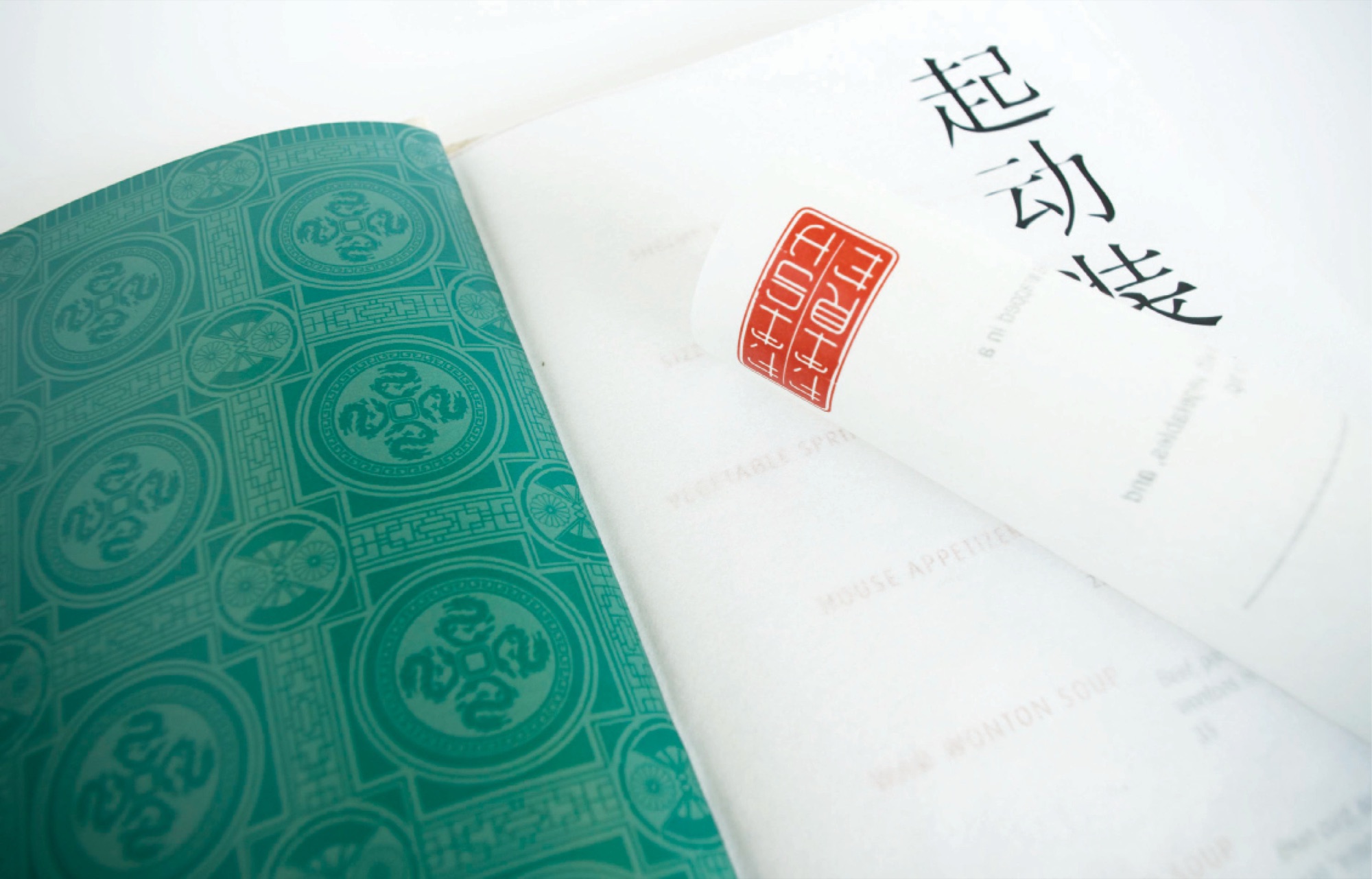 A menu opened flat: the endpaper printed with a green dragon-roundel pattern, the facing page carrying brushed Chinese characters and a red seal above the dish list